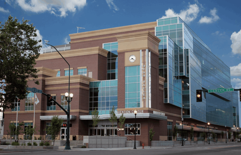 A modern brick-and-glass convention center in Utah stands at a sunny city intersection.